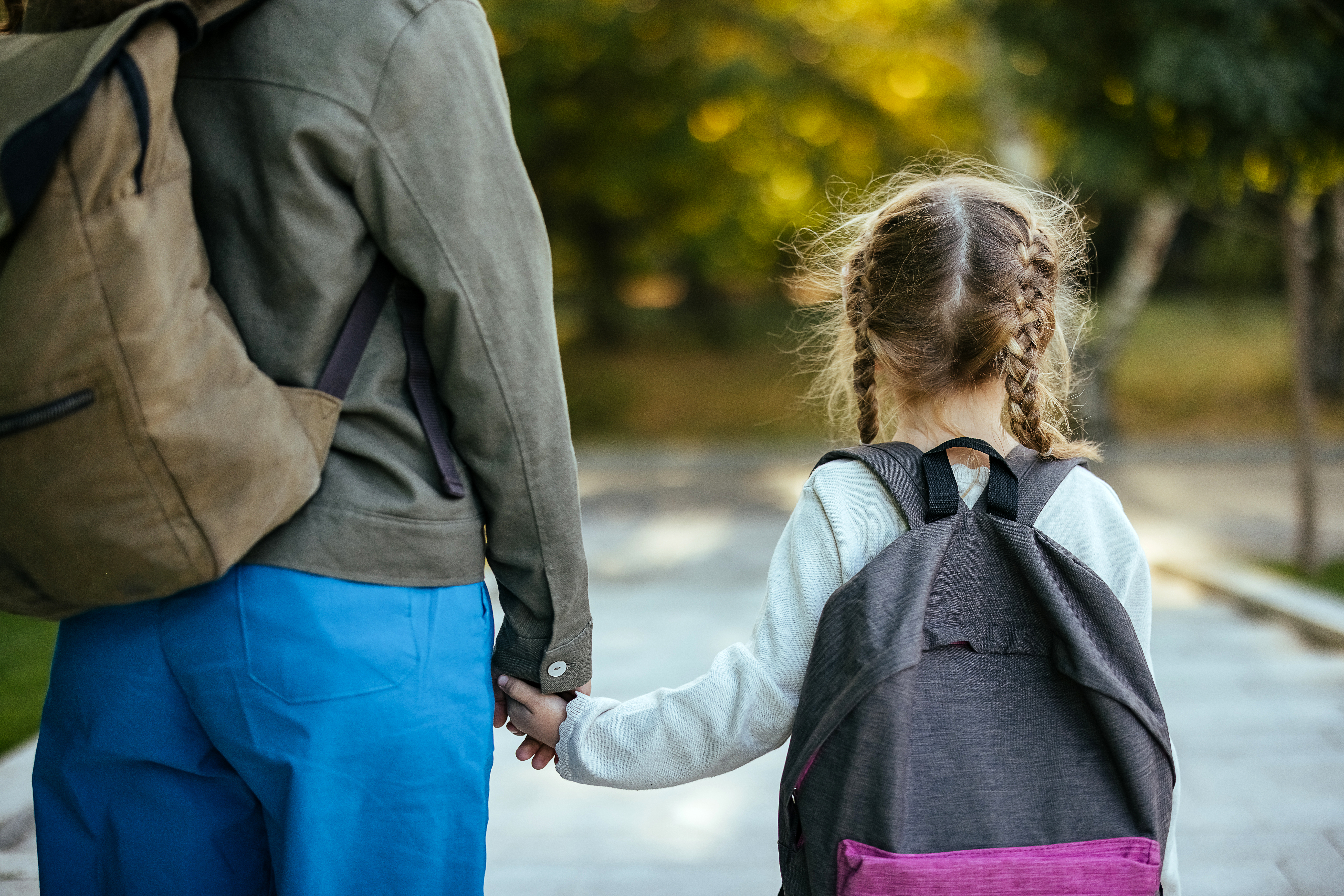 A woman and child with braided hair wearing backpacks, holding hands and walking together